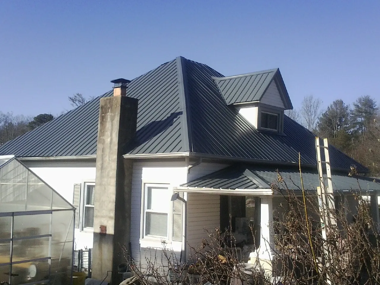 Dark blue standing seam metal roof on a white farmhouse with dormer — Slate & Tile Roof Repair by Roofing Brothers in Colliers