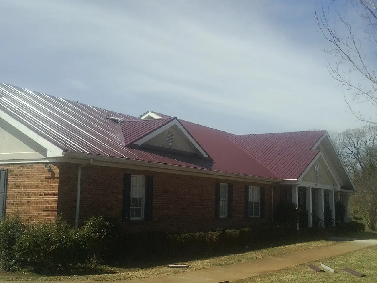 Red metal roof with gabled entries on a long brick building, from a Hail Damage Roof Repair job in Colliers