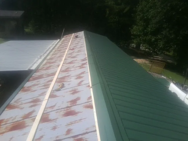 Old rusted panels beside newly installed green metal roofing — Wind Damage Roof Repair by Roofing Brothers in Colliers