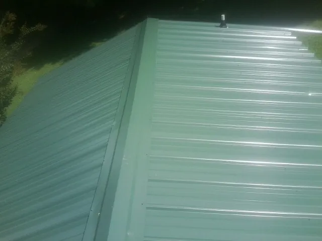New green metal panels meeting at the ridge of a roof — Flat Roof Repair work by our crew in Colliers