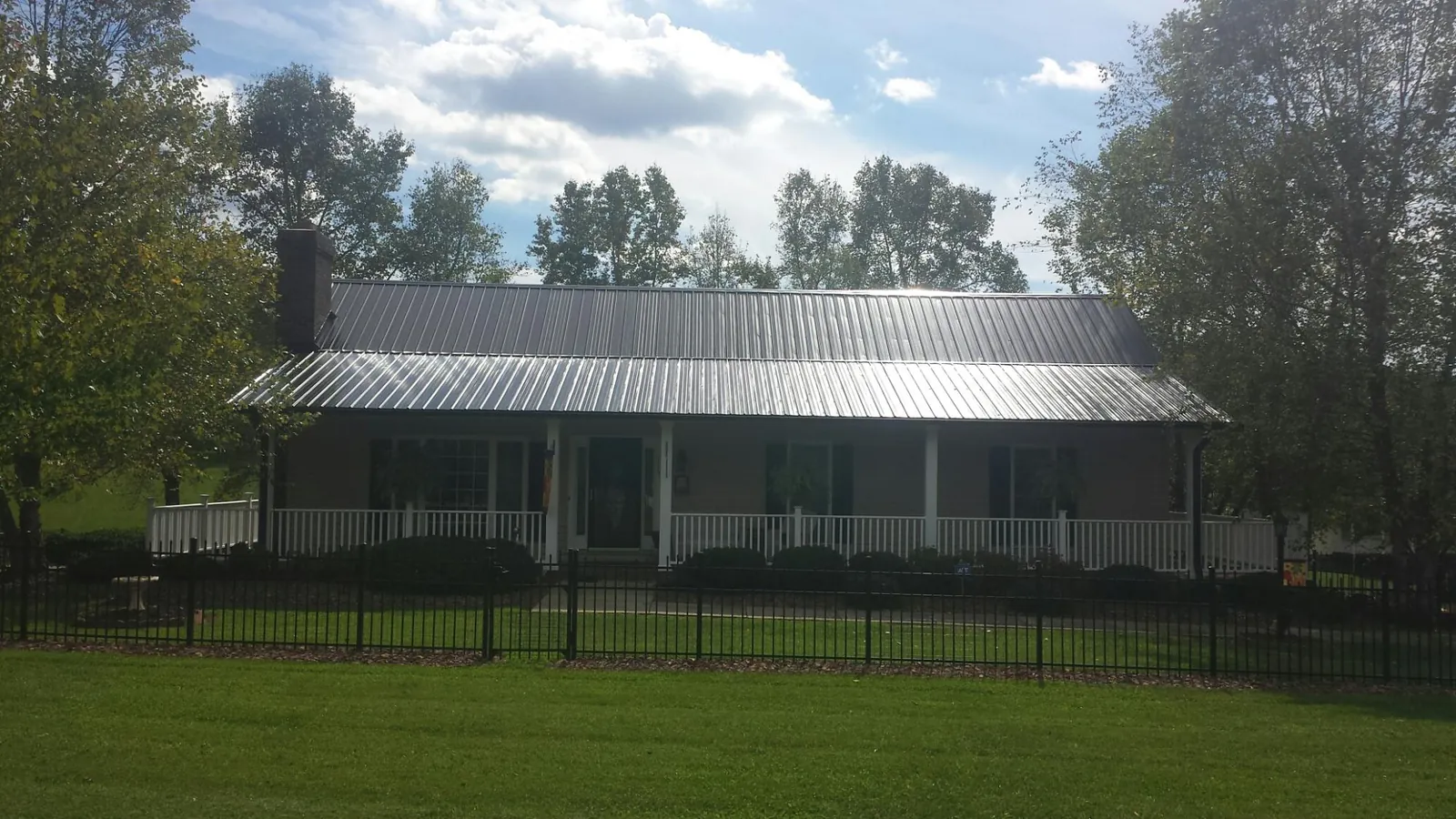 Gray metal roof on a brick ranch with a full width front porch — Gutter Guard Installation work by our crew in Colliers