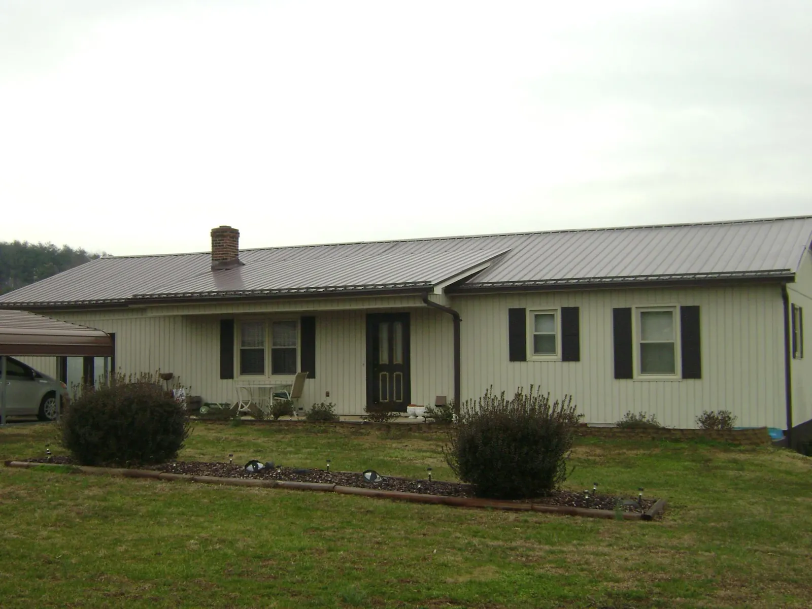 Brown metal roof on a cream sided ranch home with a brick chimney in Colliers