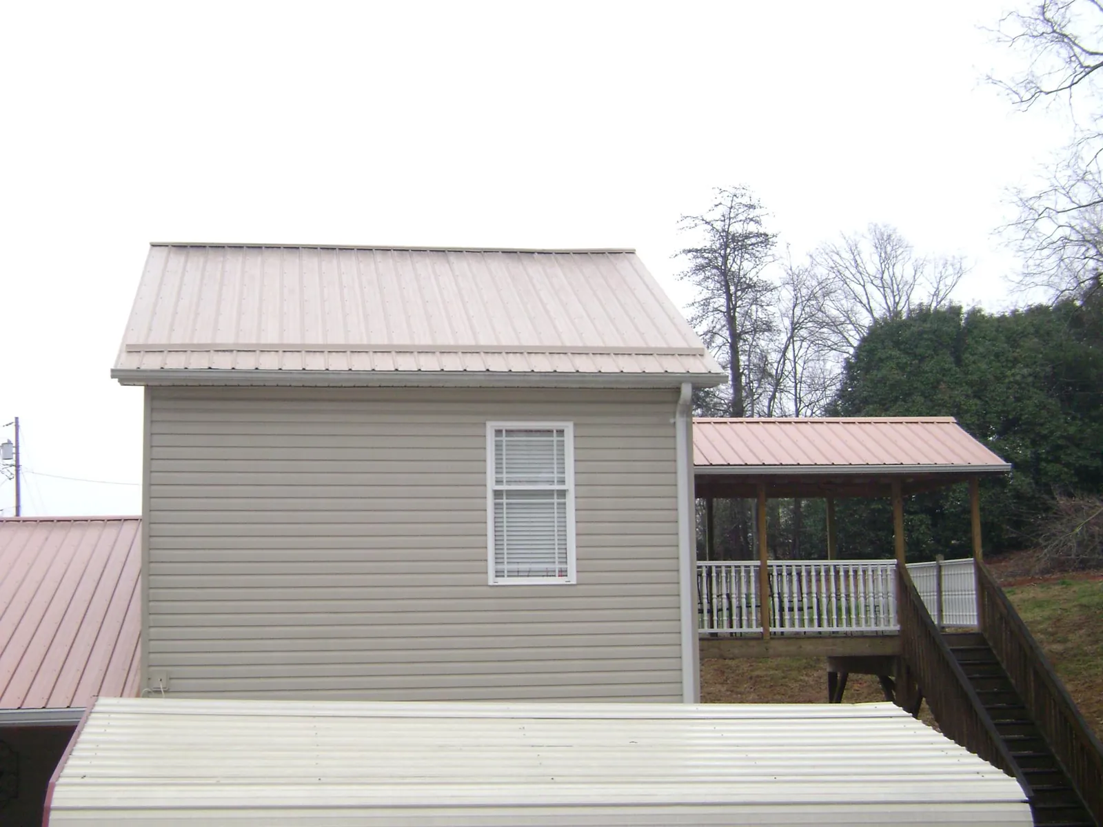 Tan metal roofs on a two story addition and attached porch, from a Roof Replacement job in Colliers